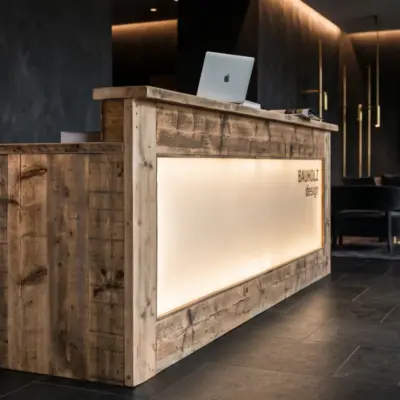 Beleuchtete Empfangstheke aus massivem Altholz von BAUHOLZ design in einer dunklen, luxuriösen Lobby